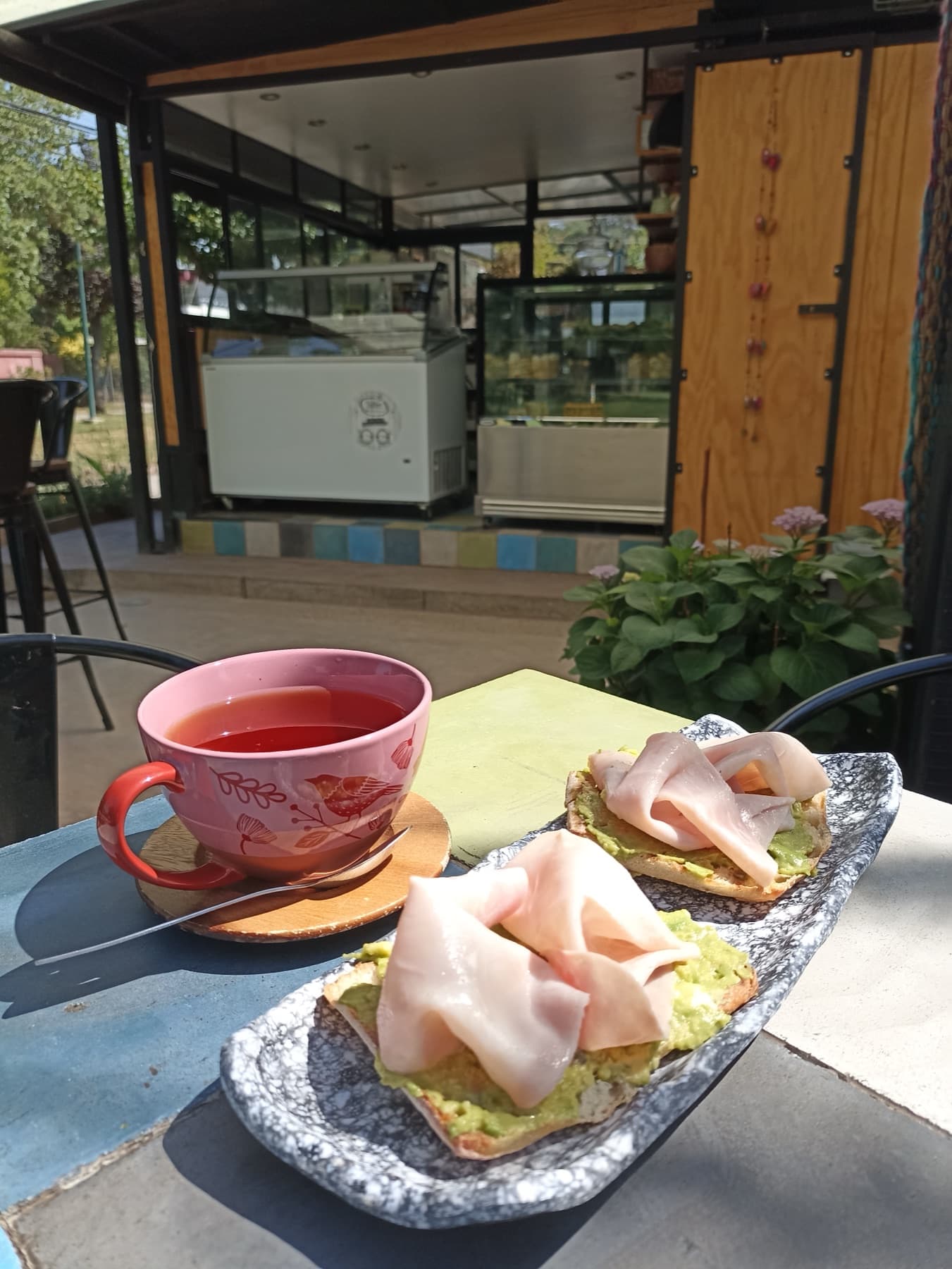 Tostadas con palta y jamón, y un té, en una mesa de la terraza